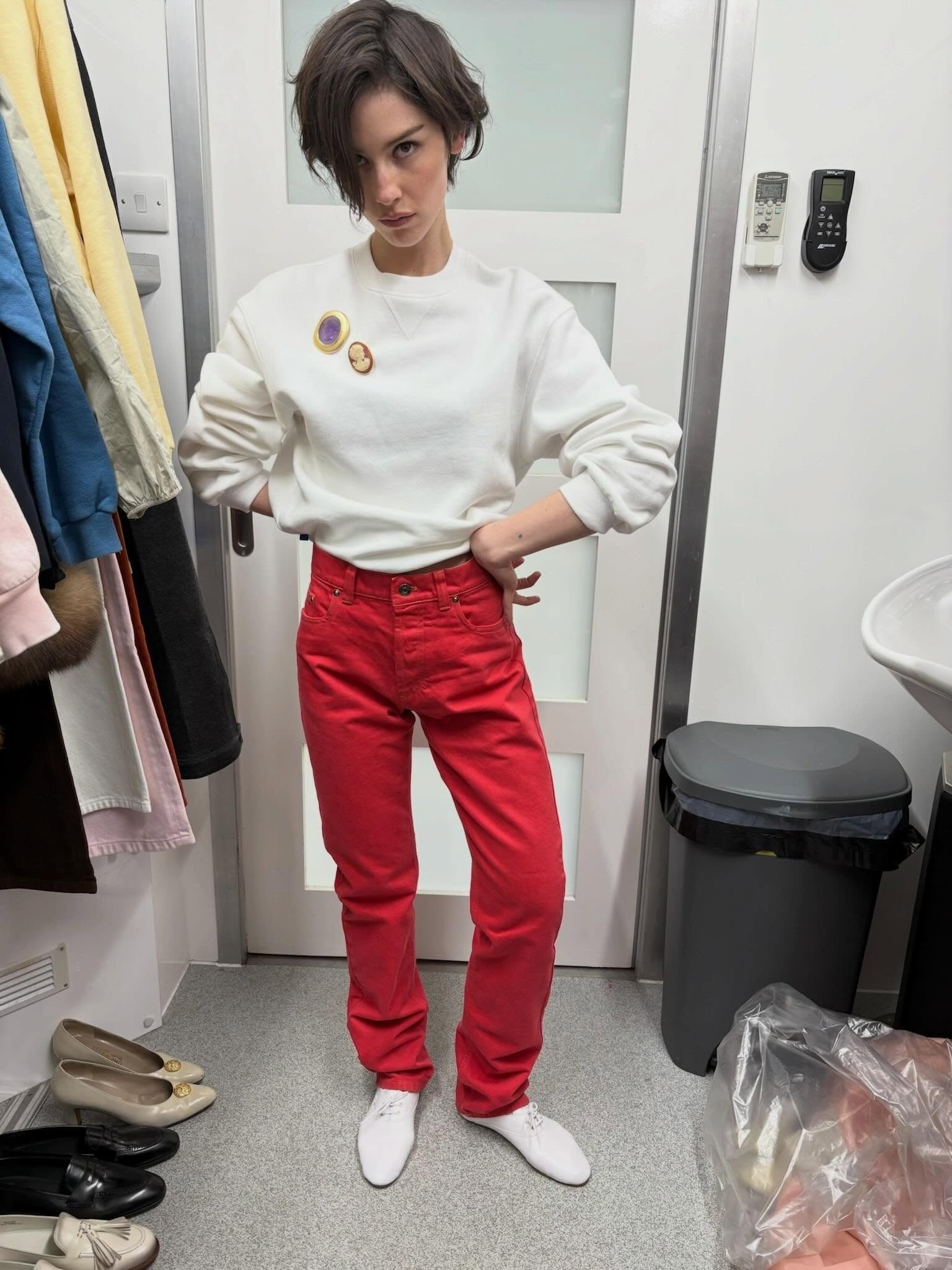 Gracie Abrams wearing a cream sweatshirt, red jeans, and white oxford flats.