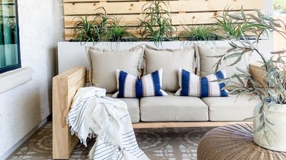A DIY outdoor sofa on decorative taupe and white patio tile flooring against wooden pallet backdrop