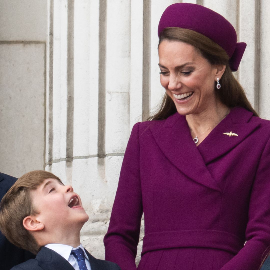 Princess Kate in a berry coat and hat, laughing looking at Prince Louis