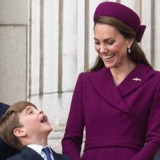 Princess Kate in a berry coat and hat, laughing looking at Prince Louis