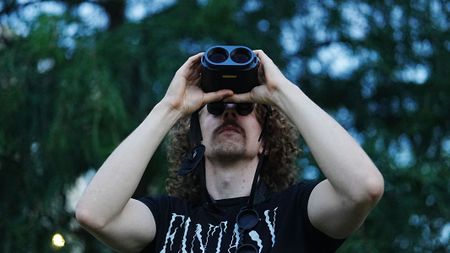 A man looking through the Fujifilm Techno-Stabi TS-L 1640 image-stabilized binoculars upwards with trees in the background.
