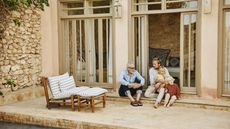 A father and adult son have a discussion while relaxing with family on a terrace.