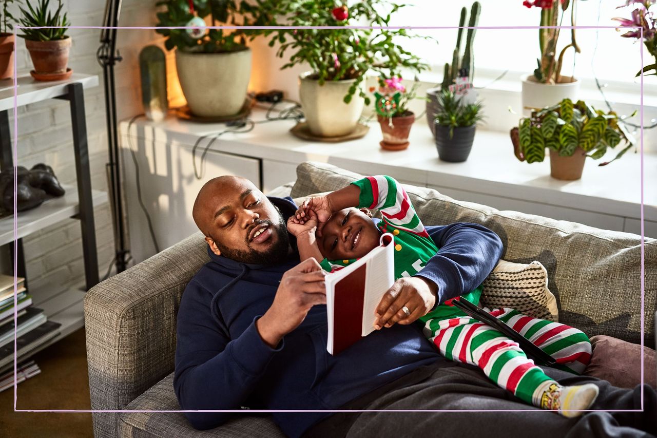 A man lying on a sofa reading to a young boy