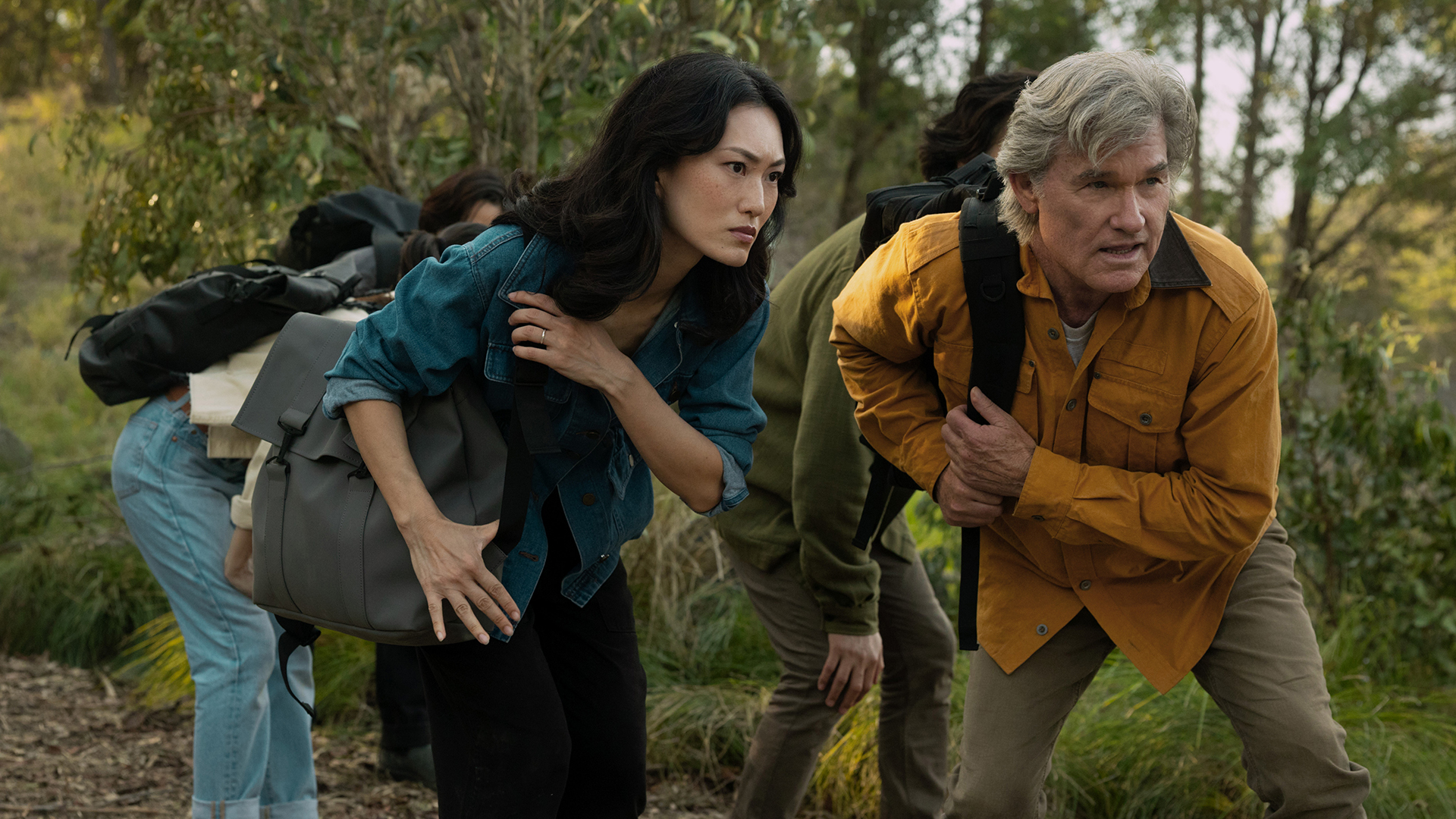 Keiko and Lee carrying rucksacks and bent over in a forest in Monarch: Legacy of Monsters season 2 episode 5
