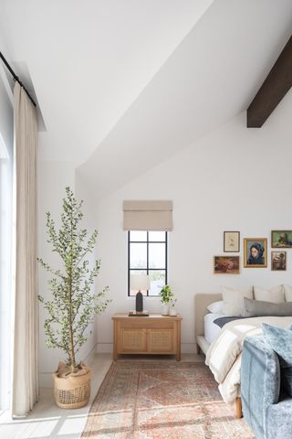 white bedroom with tall ceiling, plant and art