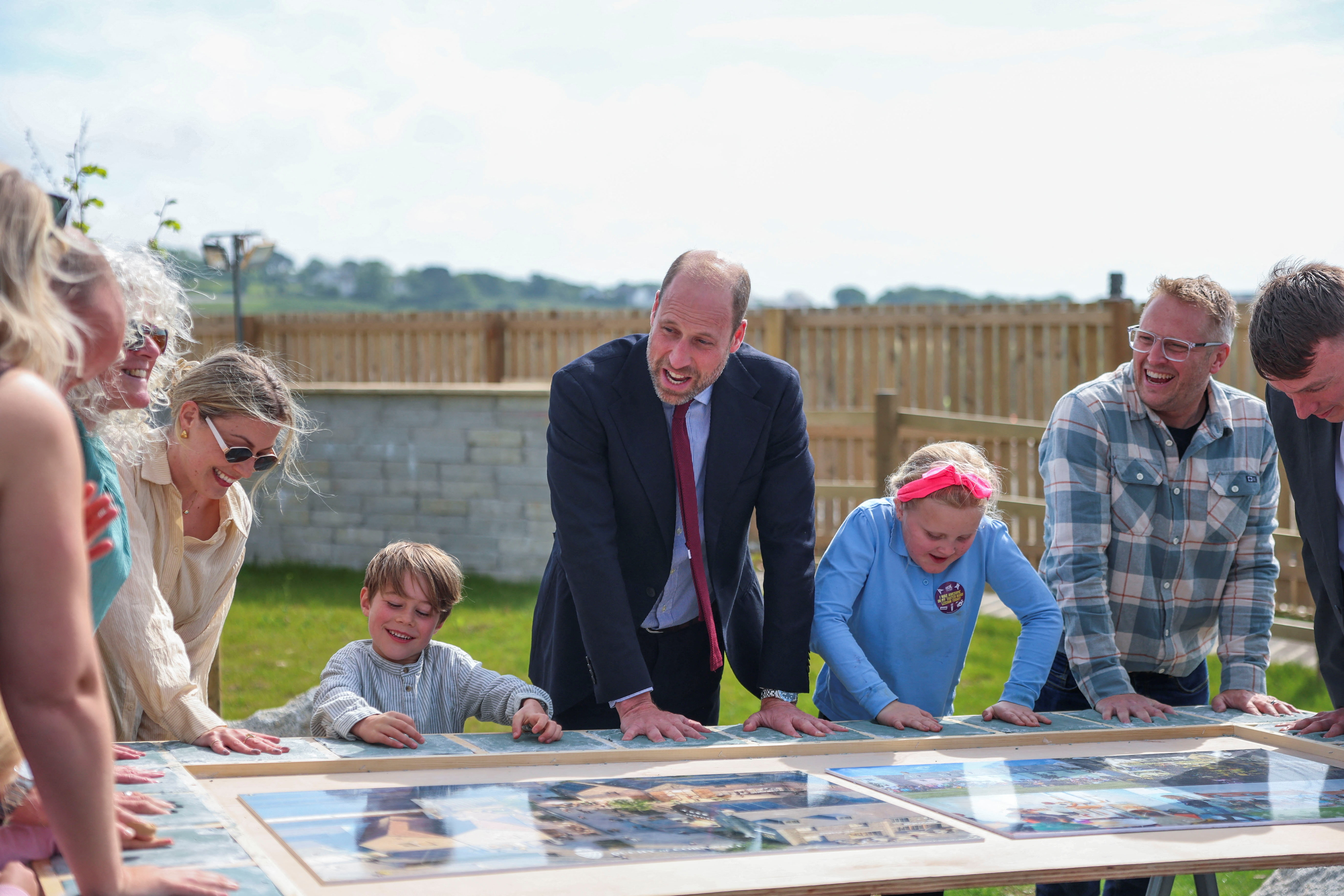 Prince William standing with kids and parents around a table with photos