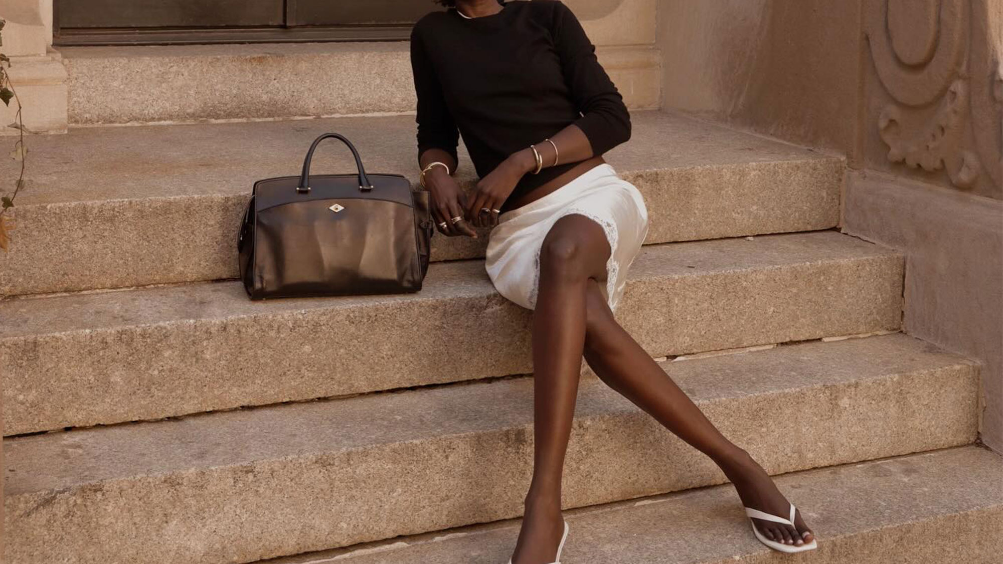 Woman wearing a black crewneck, a cream slip skirt, and white flip-flops.