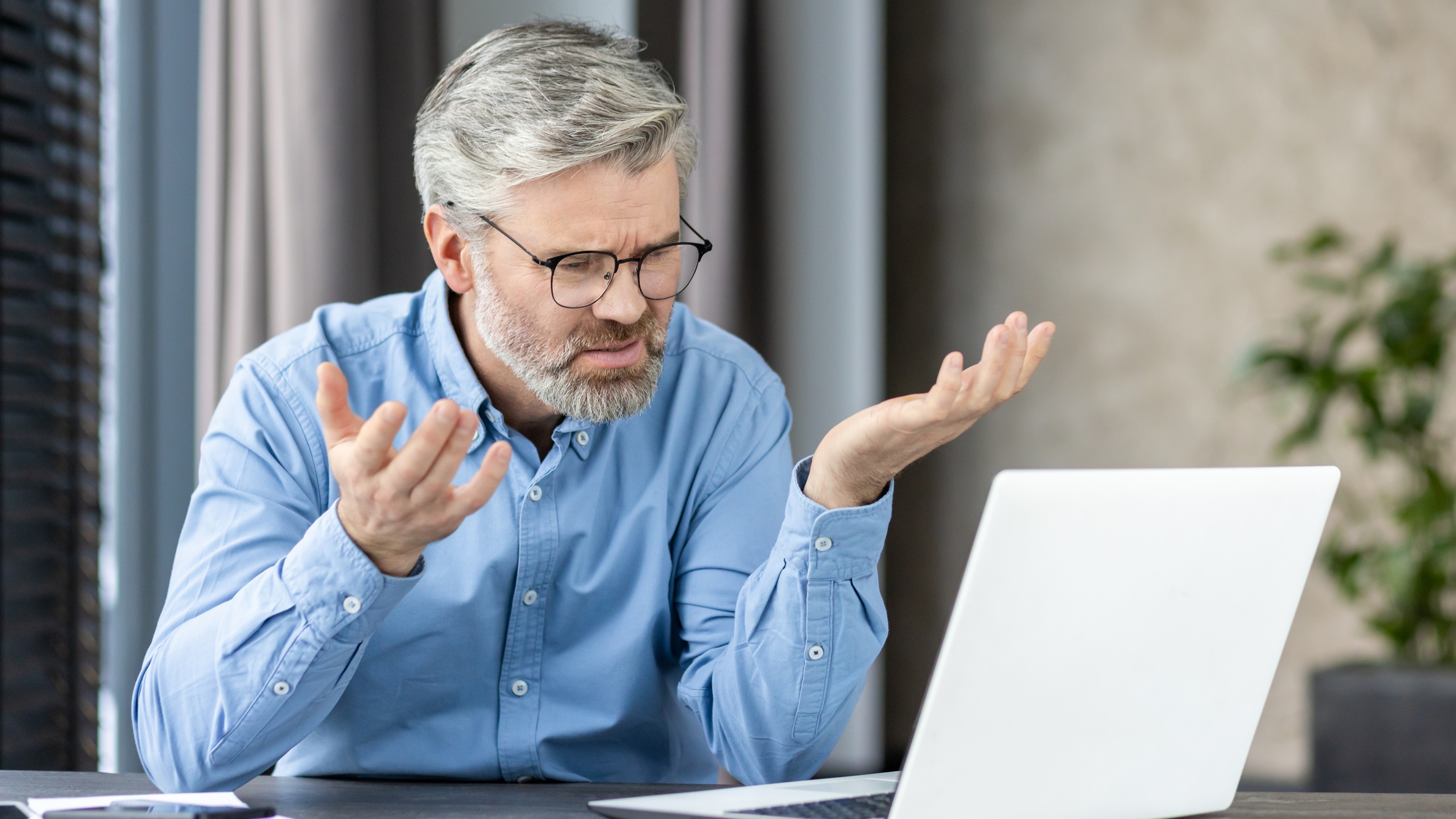 An older businessman looks upset as he looks at his laptop at his desk.