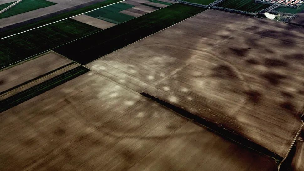 a view of farmland shows a faint outline of a round settlement with brighter patches in the center.