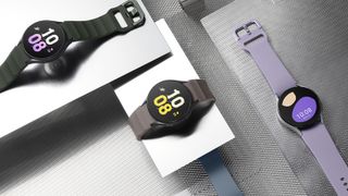 Tre stycken Galaxy Watch 5-modeller ligger utplacerade på ett grått bord.