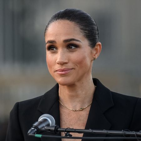 Meghan Markle wearing a black suit giving a speech in a mic