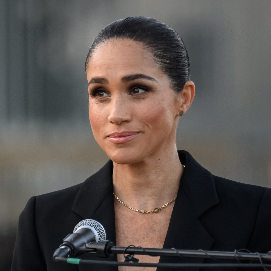 Meghan Markle wearing a black suit giving a speech in a mic