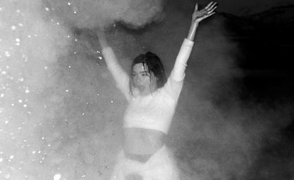 Bjork wearing white crop top with arms in the air in the rain.