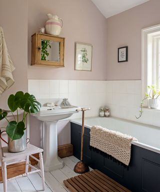 Pink painted bathroom with white tiles and painted bathtub, plants and wooden accessories