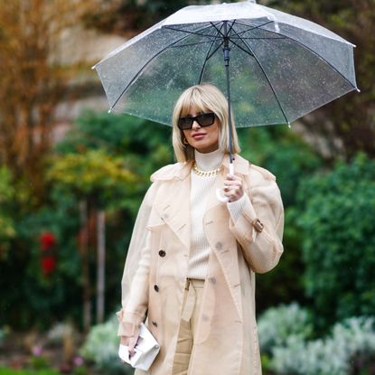 Xenia Adonts wears sunglasses, a white turtleneck pullover, a golden chain necklace, a beige clear long rain jacket, beige pants, outside Maison Margiela, during Paris Fashion Week - Womenswear Fall/Winter 2020/2021, on February 26, 2020 in Paris, France. 