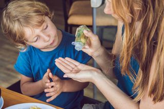 A woman putting hand sanitizer on her hand to give to a young boy. 