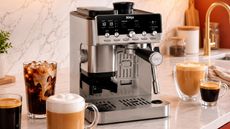 Ninja Luxe&trade; Caf&eacute; Mini Plus AutoFroth Espresso Machine on a marble kitchen counter beside an array of glass mugs of coffee