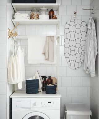 ikea boaxel shelving unit in small laundry room with small hanging ironing board, washing machine and laundry basket on white tiled wall