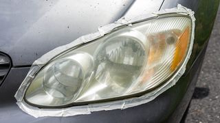 A grey car which has masking tape around its headlight