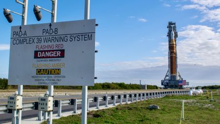 An orange rocket with a white top stands against a dynamic sky. A danger sign stands on the left.