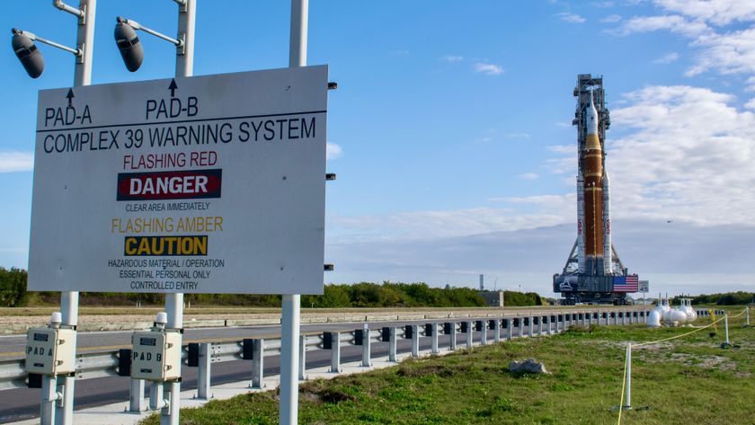 An orange rocket with a white top stands against a dynamic sky. A danger sign stands on the left.