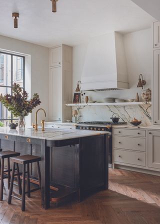 A modern white kitchen with a black freestanding island and marble backsplash