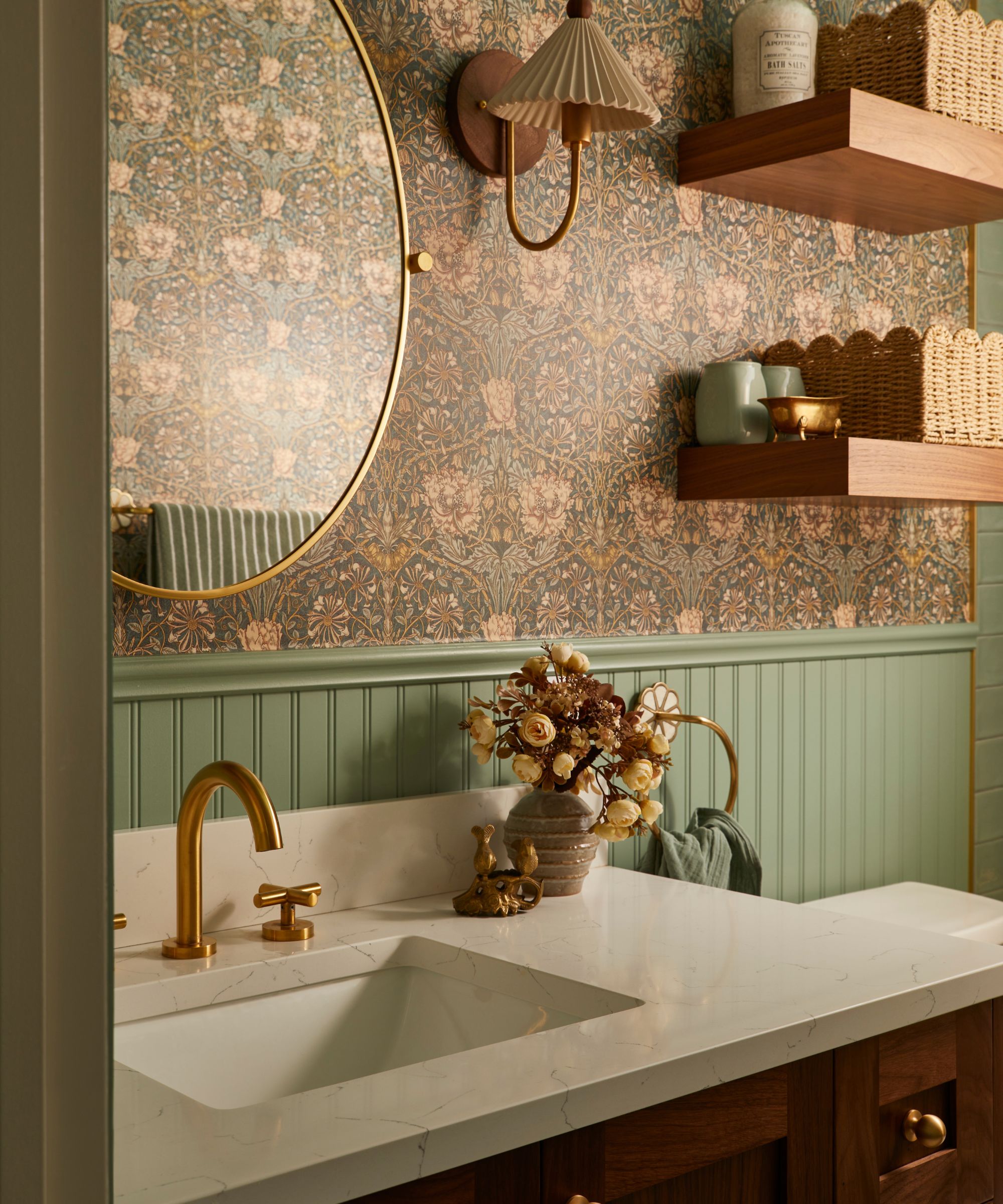 a main family bathroom with green beadboard paneling, a marble and wooden vanity, floral william morris wallpaper and floating shelving