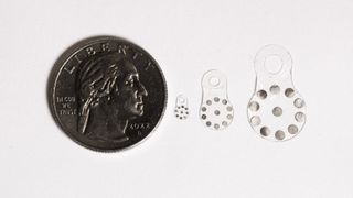 A picture of three different-sized versions of the new implantable device, called BioSUM, lined up side to side next to a coin for scale. A white background is shown.