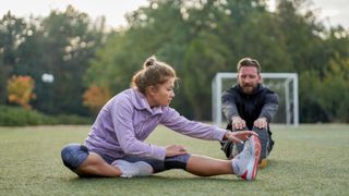 Woman in her 50s stretching with male friend wearing active clothes on football field, showing the benefits of running for women