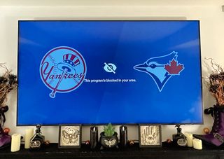 A TV above a mantle-place with a graphic revealing the Yankees vs Blue Jays game is blocked in this region.