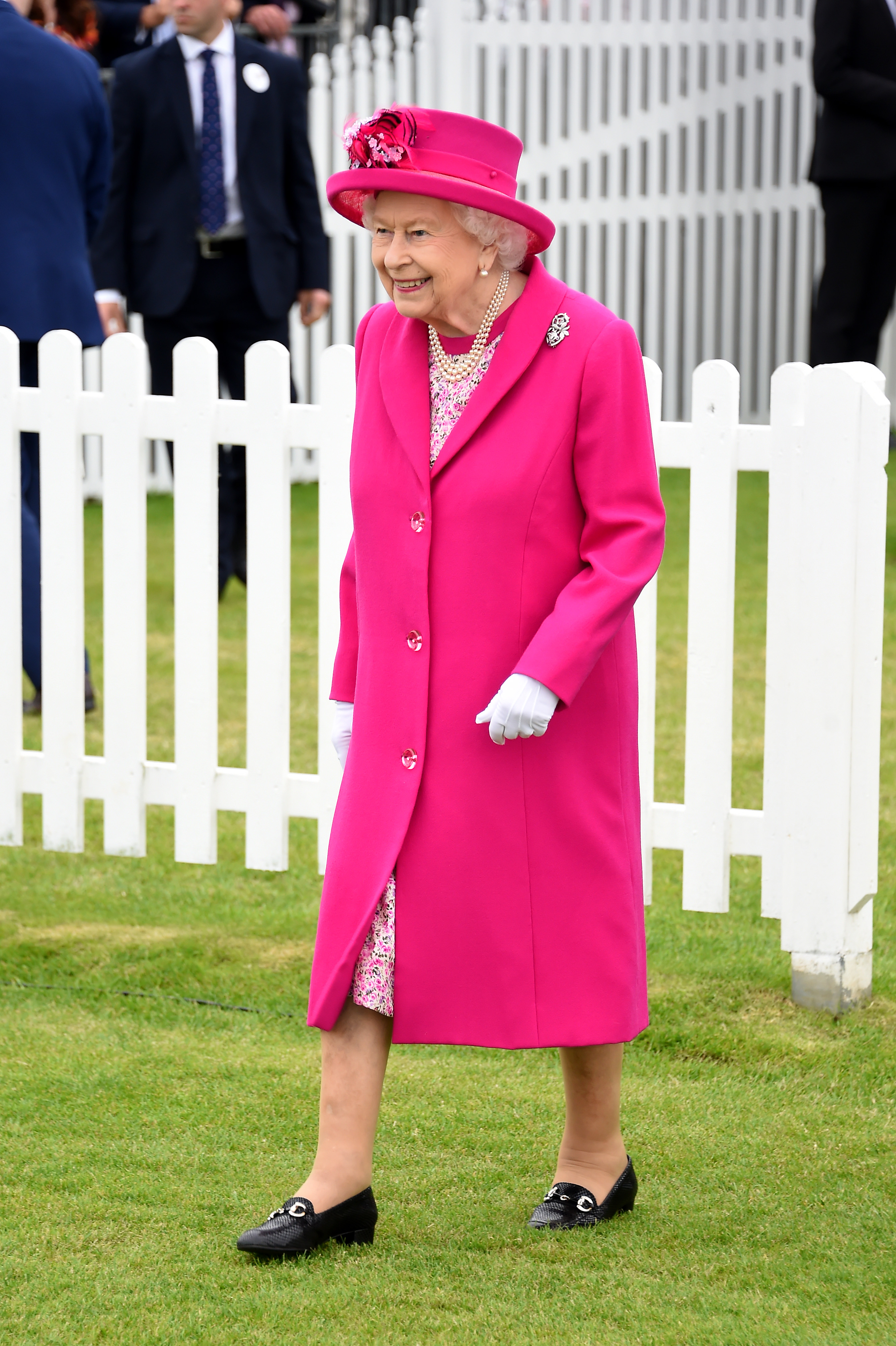 Queen Elizabeth in a pink coat and hat walking on a field