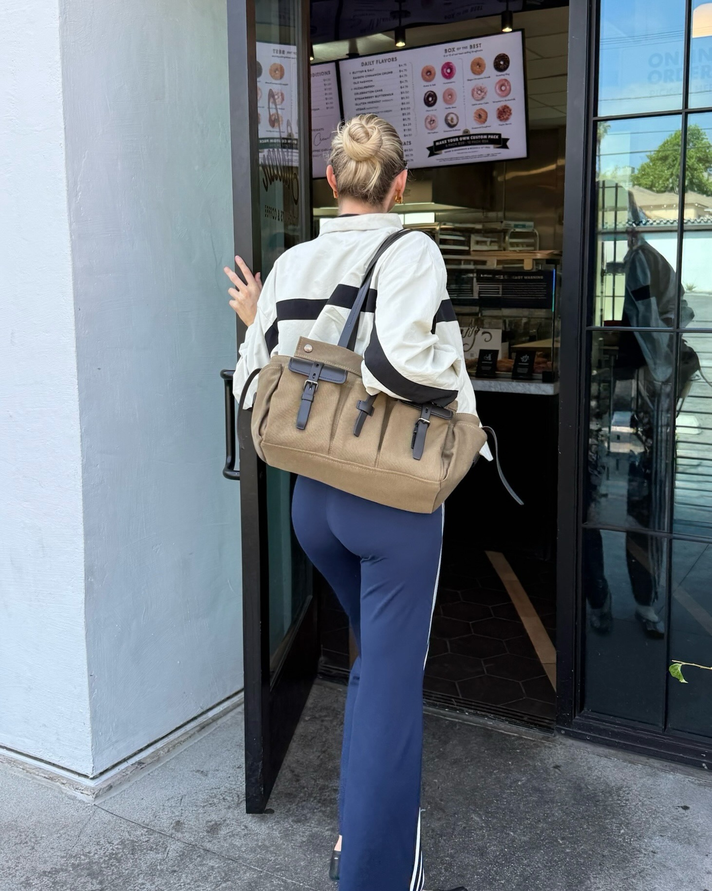 Elsa Hosk wearing a windbreaker, a camo T-shirt, Adidas track pants, Maison Margiela Tabi ballet flats, and a Prada Route bag.
