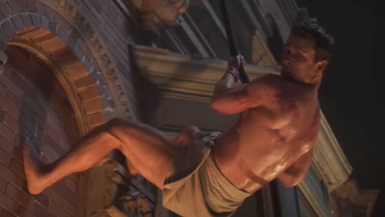 Glen Powell wearing only a towel around his waist while hanging on the side of a building in The Running Man.