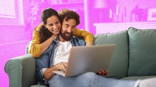 Young couple looking happy whilst looking at laptop on the sofa.