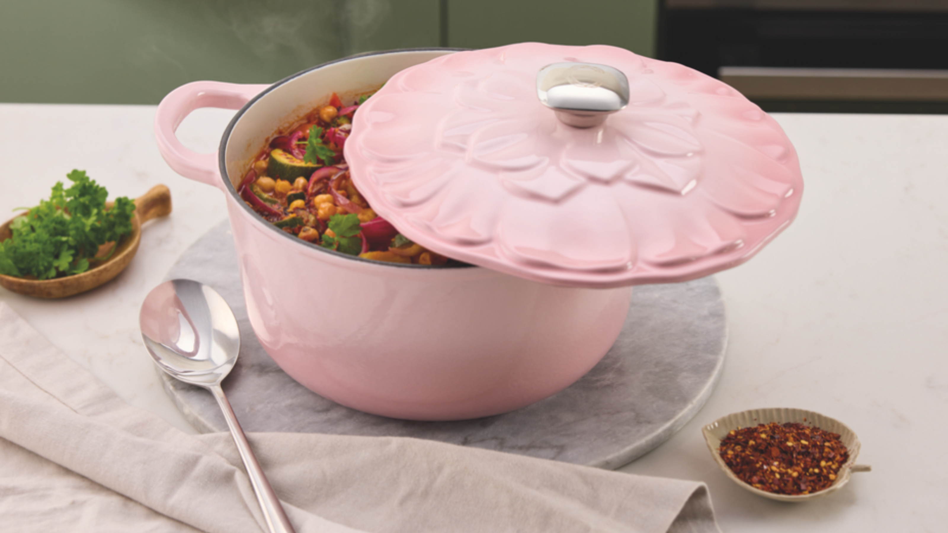 Aldi pink cast iron petal caserole on white kitchen countertop, filled with vegetable stew.