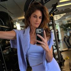 Cindy Crawford takes a mirror selfie at the gym wearing cornflower blue leggings, tank top and a jumper.