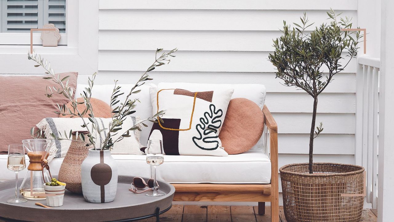 patio area with white clapboard house exterior with sofa and potted Aldi olive trees