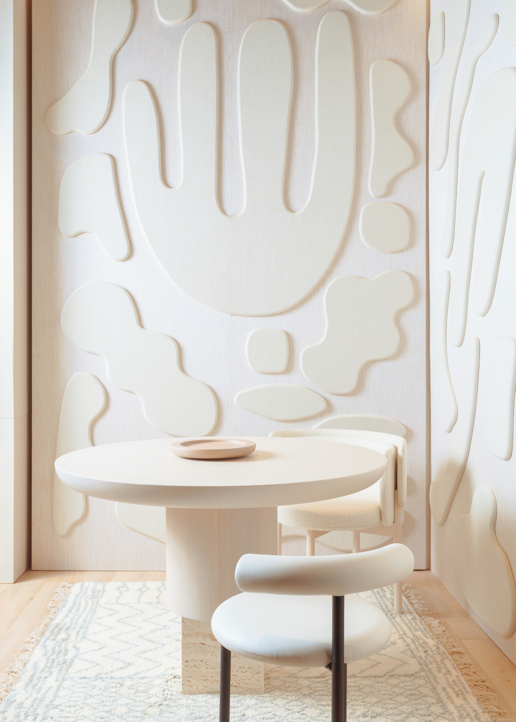 an all cream dining space with round table and two modern bolster chairs with modern wall molding designs