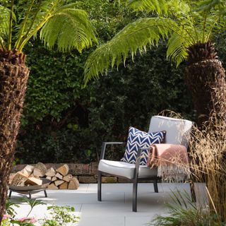Palm trees on a light stone paved patio creating shade above a white outdoor armchair