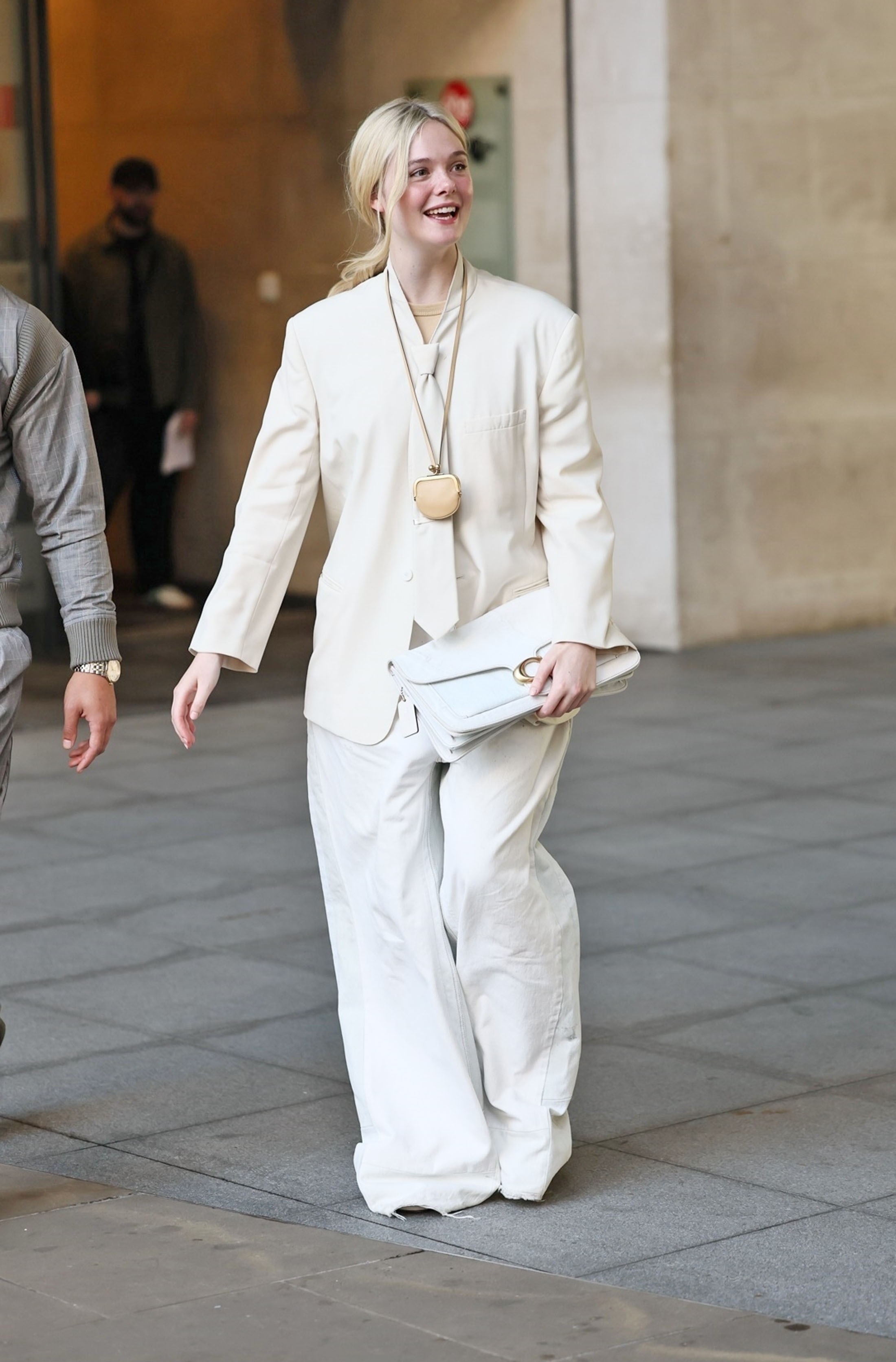 Elle Fanning wears a white oversized suit with a purse necklace and a white Coach bag.