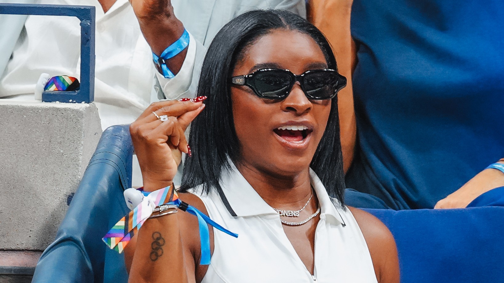 a woman with short black hair wearing a white top and black sunglasses at a sporting event