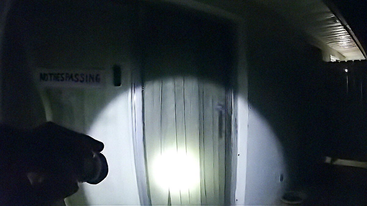 A hand pointing a flashlight at a door in Netflix documentary The Perfect Neighbor.
