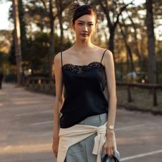 woman wearing black lace camisole, gray trousers, white sweater. 