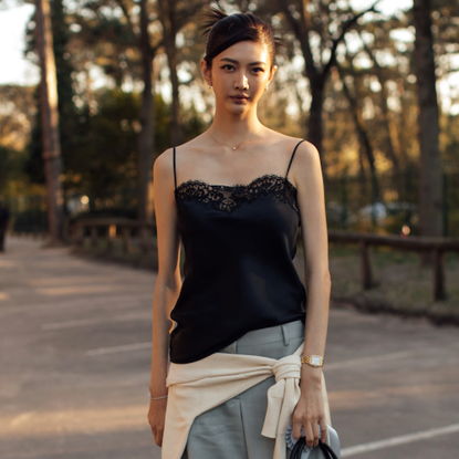 woman wearing black lace camisole, gray trousers, white sweater. 