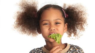 A smiling girl has a mouthful of lettuce.