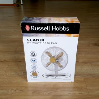 The Russell Hobbs 12” Scandi Desk Fan in a box on a wooden floor