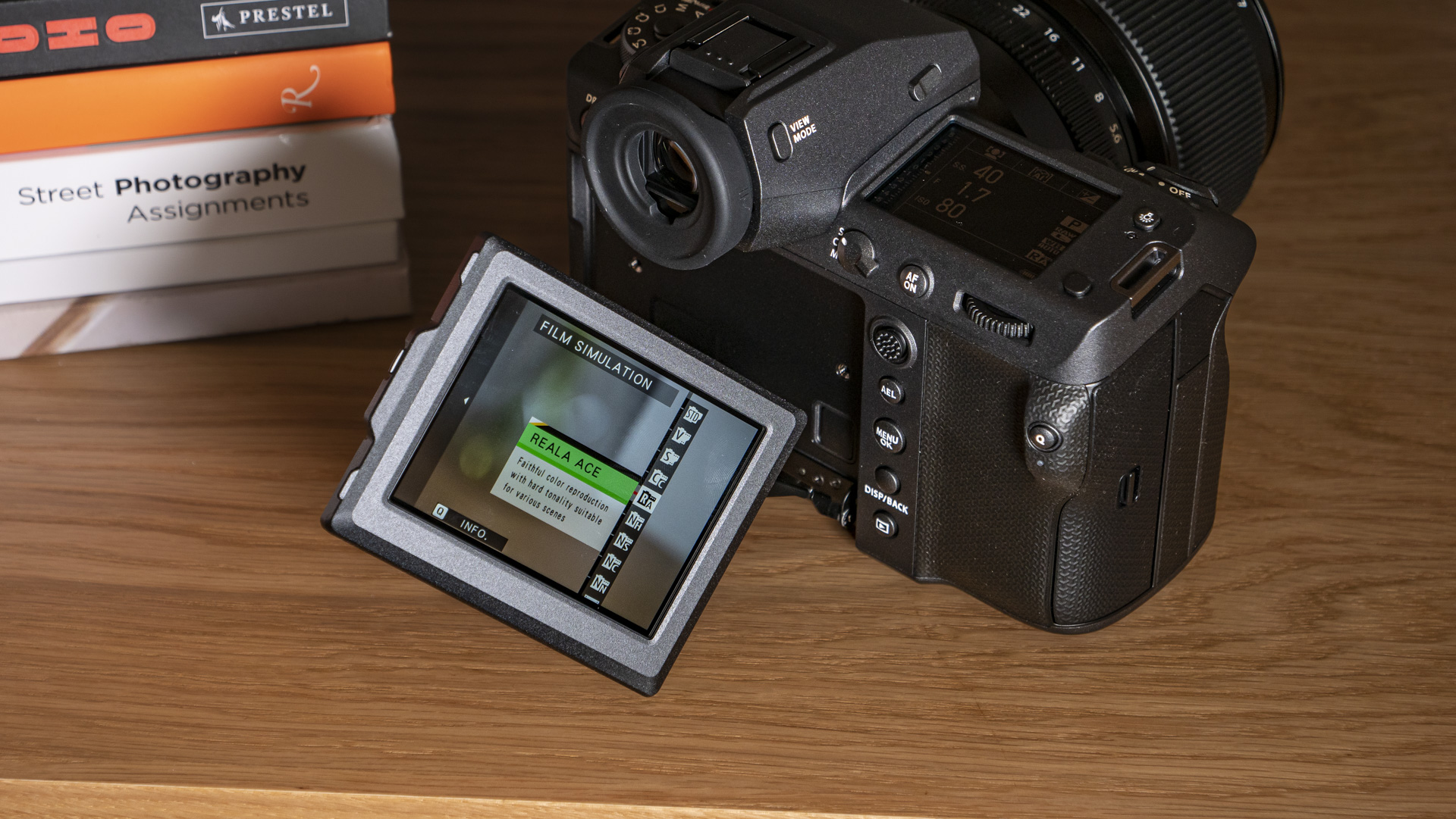 Fujifilm GFX100 II on a wooden table with new Reala Ace film simulation selected on 3-way tilt-LCD screen