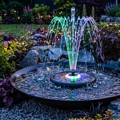 DIY water feature made with a container and an LED floating solar fountain in the garden