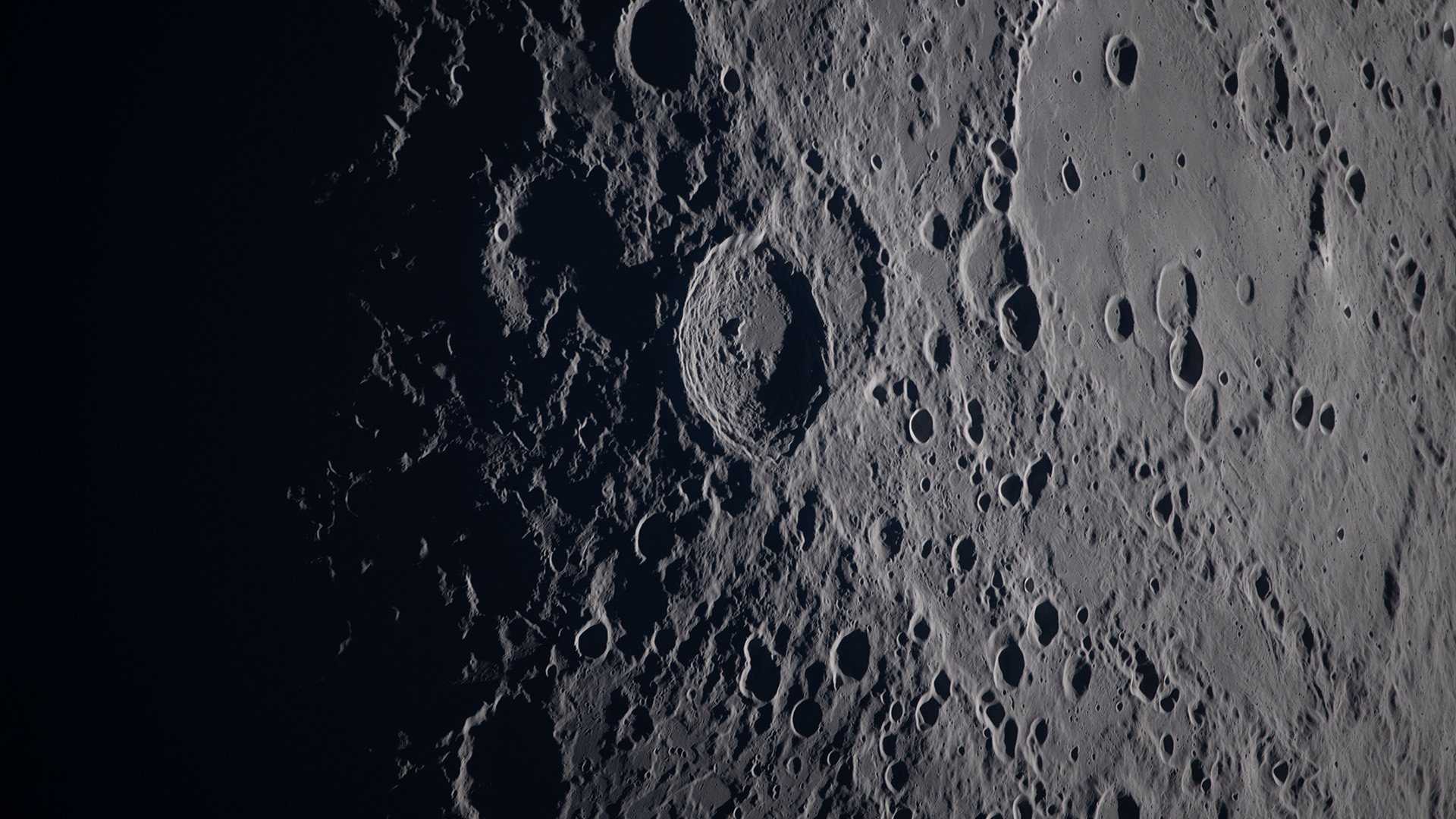 A close up of various craters on the moon's surface, the gray rock in shadow on the left of the image.
