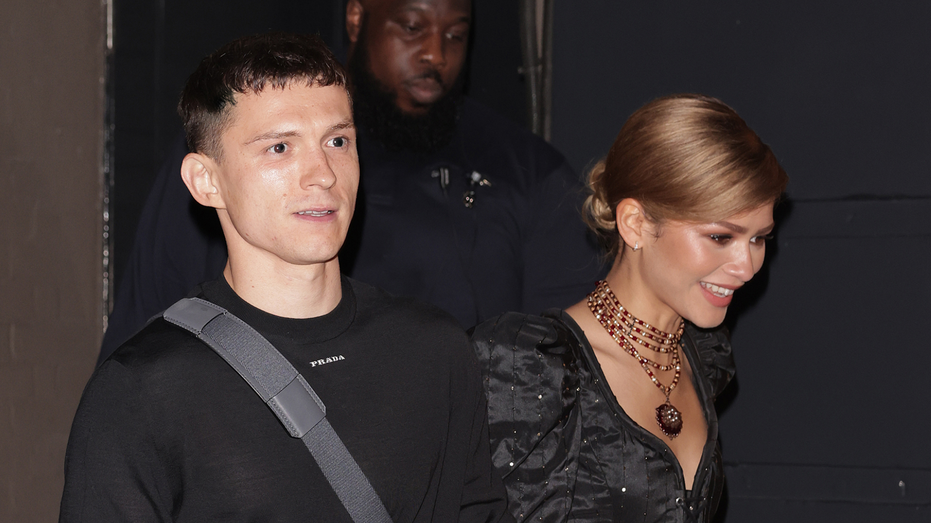 Tom Holland holds hands with fiancee Zendaya who wears a black dress